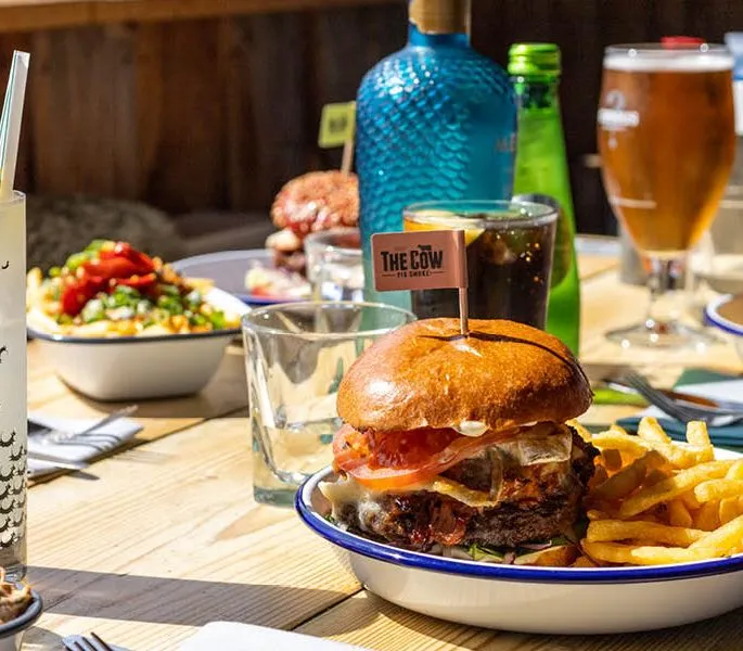 Burgers and chips with drinks on a sunlit wooden table at an outdoor restaurant