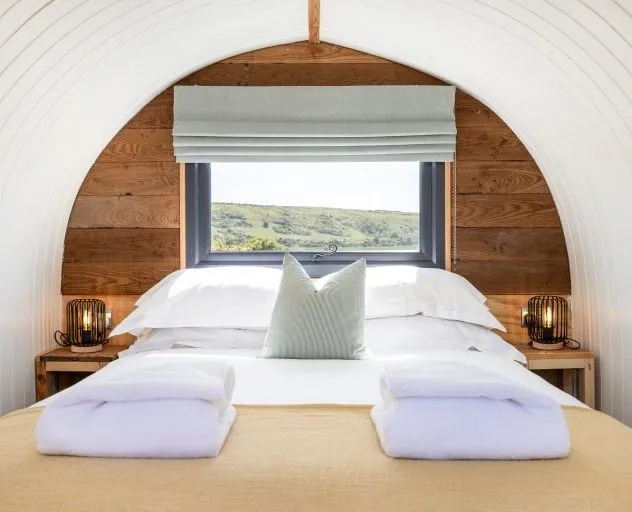 Cosy double bed in a wood-panelled cabin with a window and countryside view