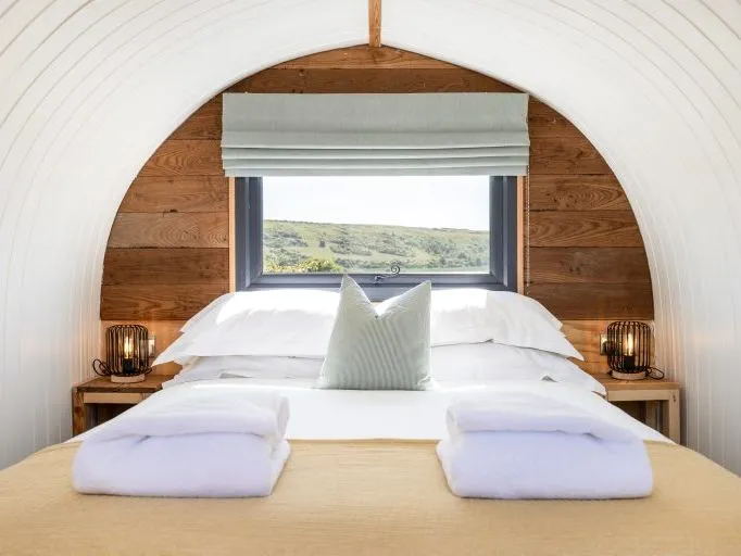 Cosy double bed in a wood-panelled cabin with a window and countryside view