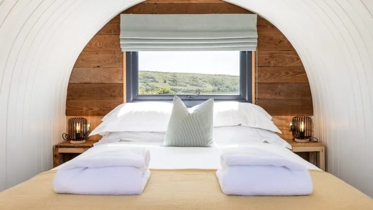 Cosy double bed in a wood-panelled cabin with a window and countryside view