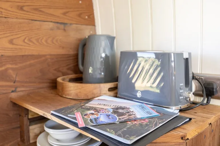 Grey toaster and jug on a wooden shelf with a magazine
