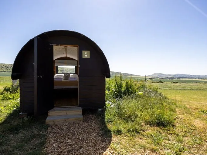 Small black camping pod with open door in a grassy field under a blue sky