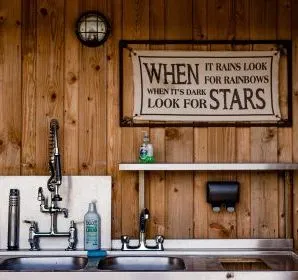Outdoor kitchen sink and taps against a wooden wall with a motivational sign above