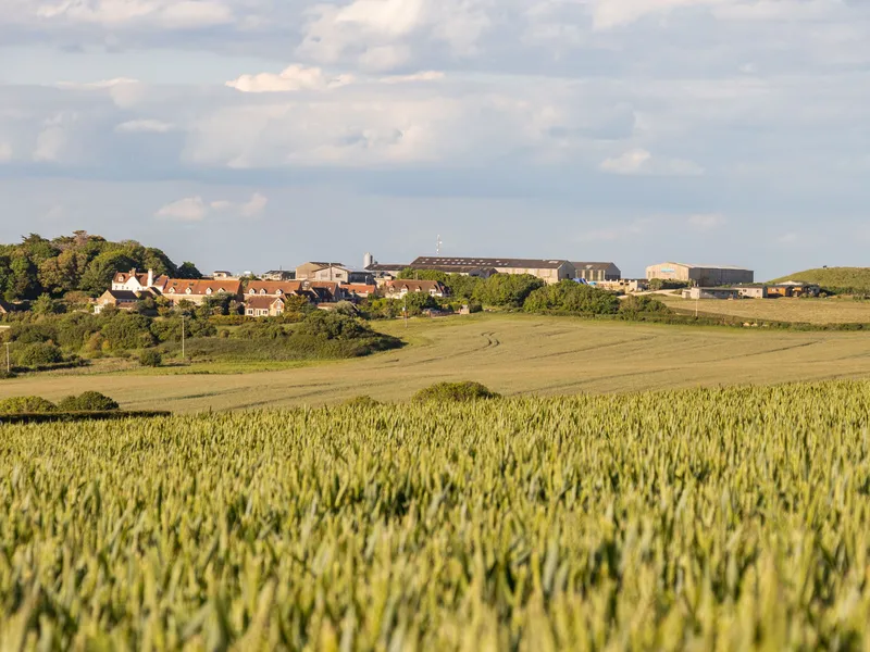 Distant view of Tapnell Farm buildings beyond green fields under a cloudy sky
