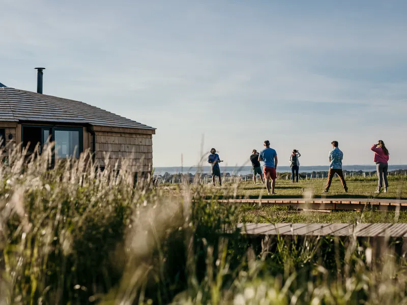 Guests standing on a grassy field beside a wooden lodge and a green geodesic dome at Tapnell Farm