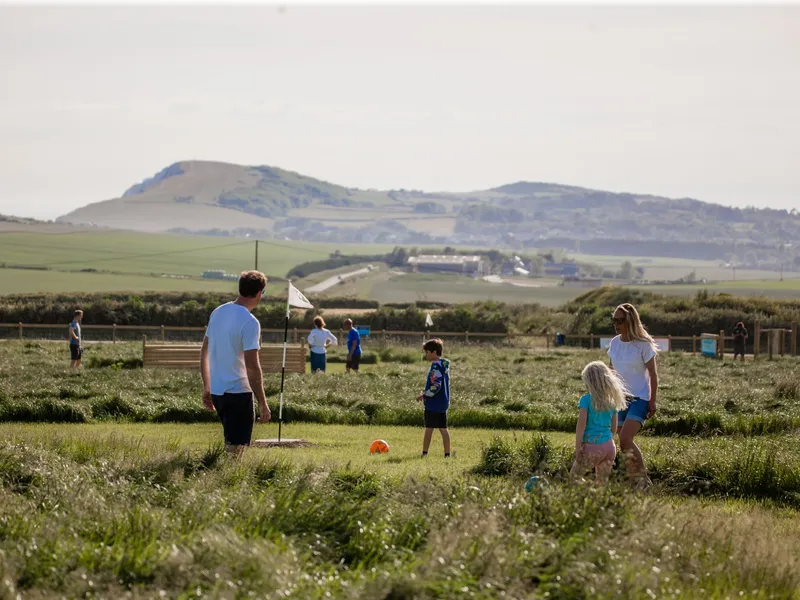 Family playing football golf on a grassy course at Tapnell Farm with countryside views in the background