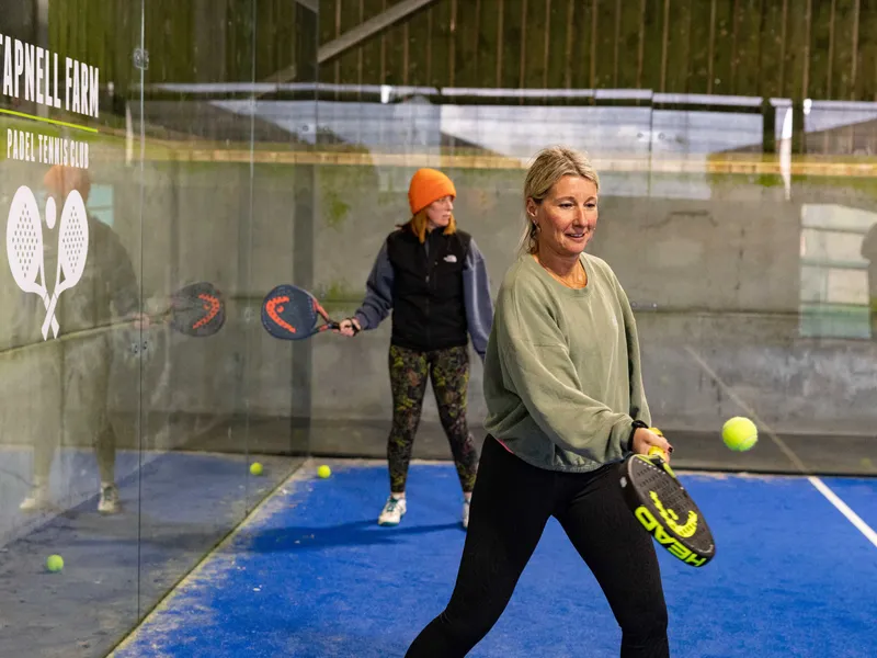 Two women playing padel on an indoor court at Tapnell Farm Padel Tennis Club