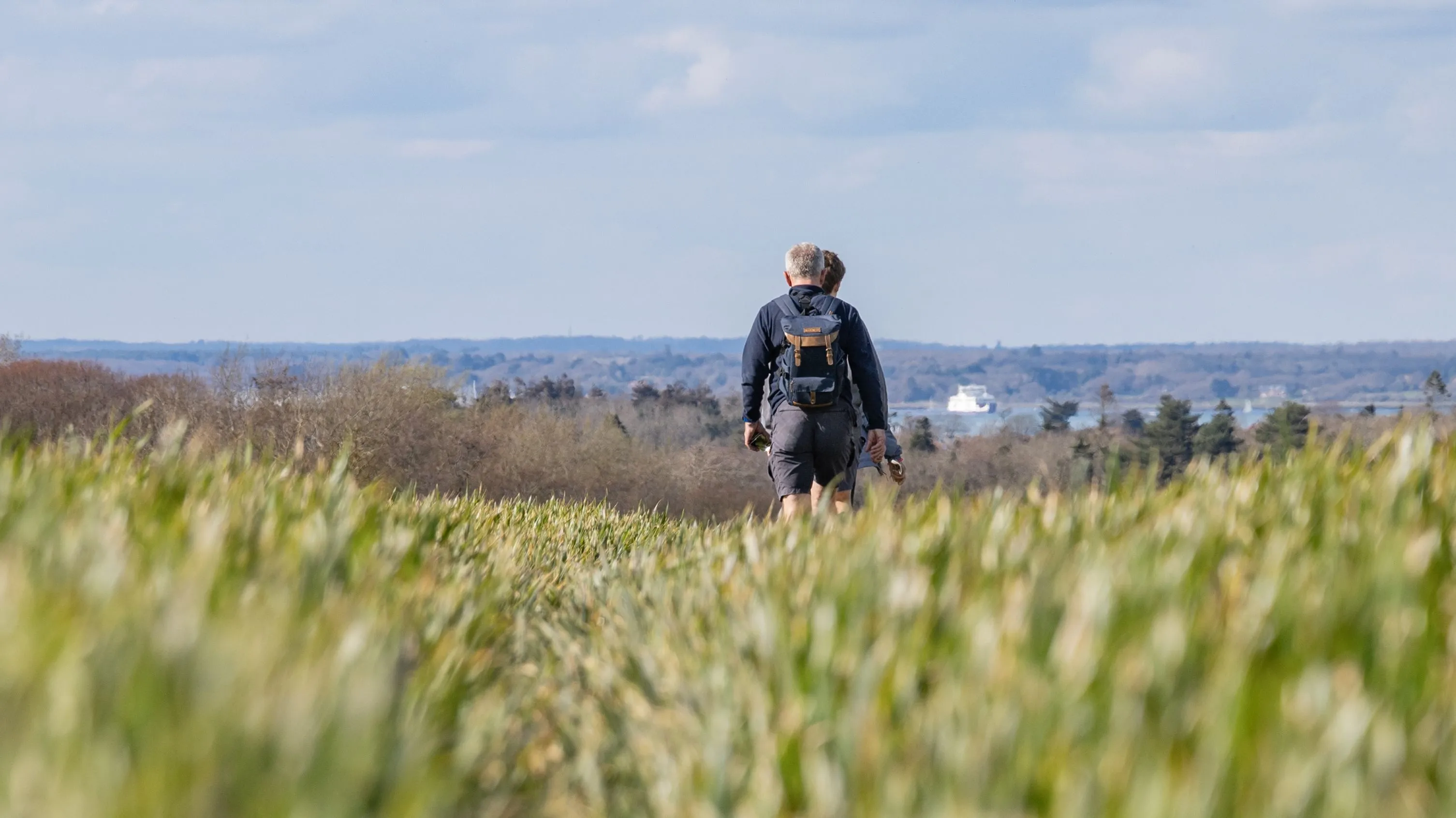 Two walkers with rucksacks crossing a grassy field on the Tapnell Trail, Isle of Wight