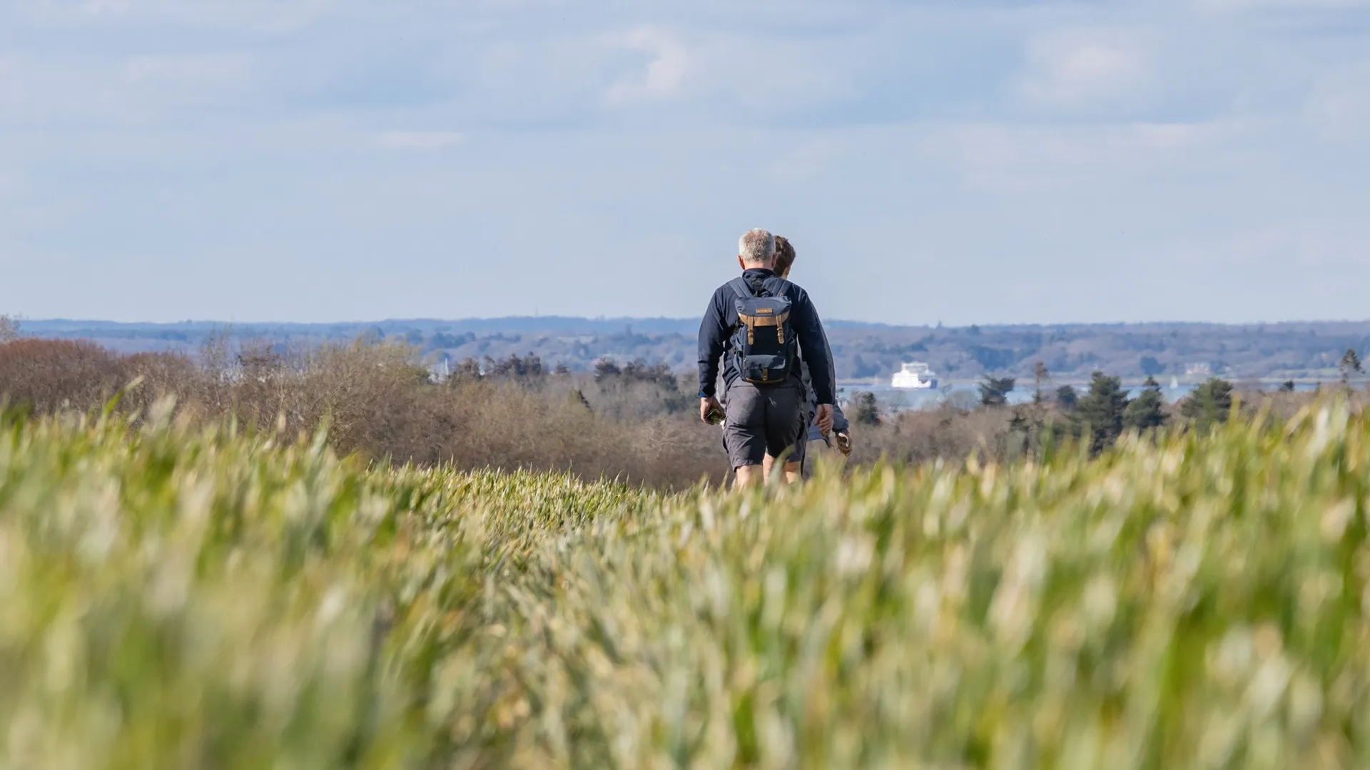 Two walkers with rucksacks crossing a grassy field on the Tapnell Trail, Isle of Wight