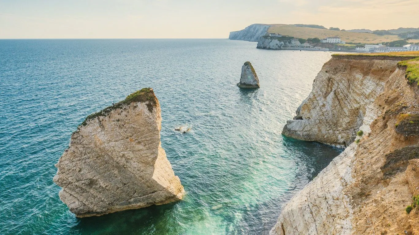 White chalk cliffs and sea stacks above turquoise water on a calm island coastline at sunset