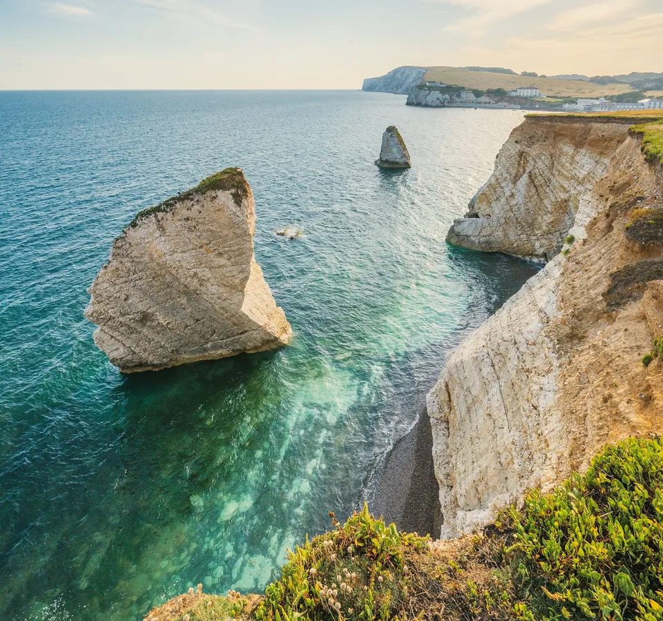 White chalk cliffs and sea stacks above turquoise water on a calm island coastline at sunset