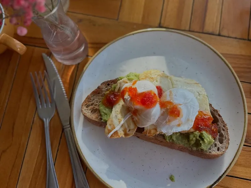 Poached eggs on avocado toast with chilli sauce on a white plate