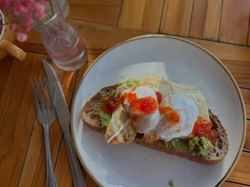 Poached eggs on avocado toast with chilli sauce on a white plate