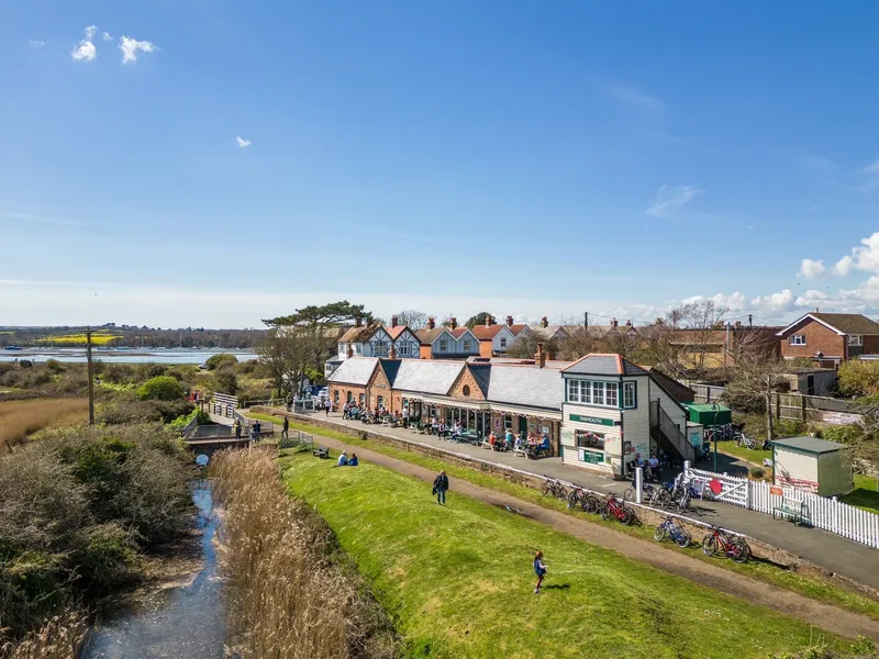 Yarmouth railway station beside a coastal marsh with bicycles and people on the platform under a bright blue sky