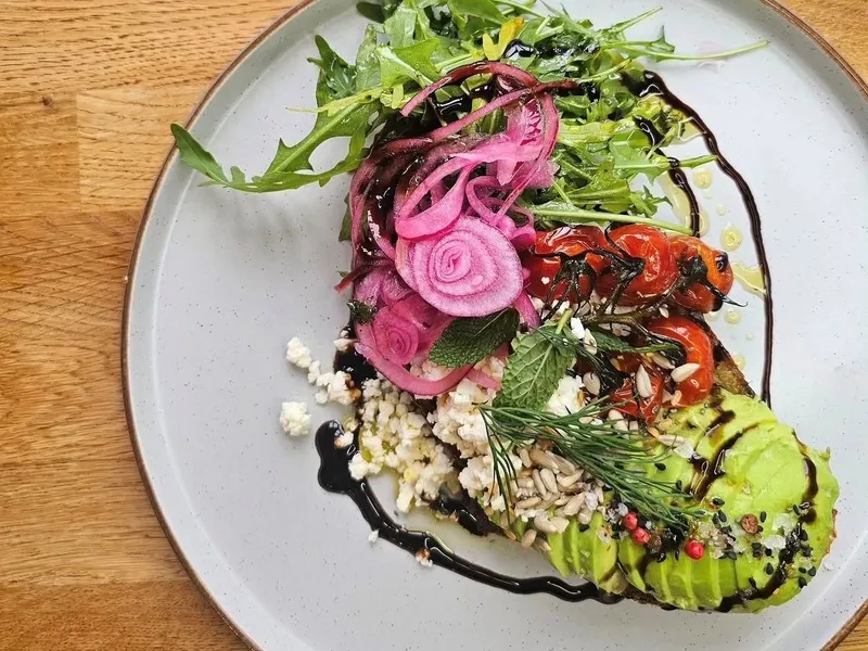Plated salad with avocado, rocket, pickled red onion, roasted tomatoes and crumbled cheese drizzled with balsamic glaze