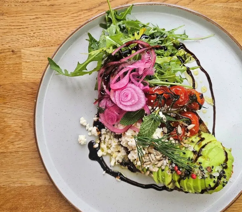 Plated salad with avocado, rocket, pickled red onion, roasted tomatoes and crumbled cheese drizzled with balsamic glaze
