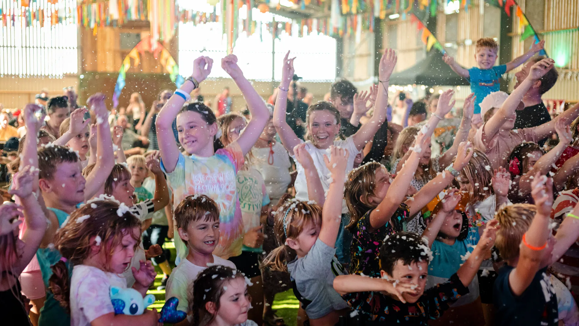 Children dancing with hands in the air at Moo Mania, with colourful bunting and foam confetti in a barn