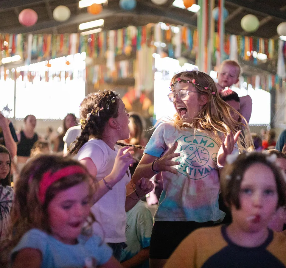 Children dancing and cheering inside a decorated barn with colourful bunting and balloons