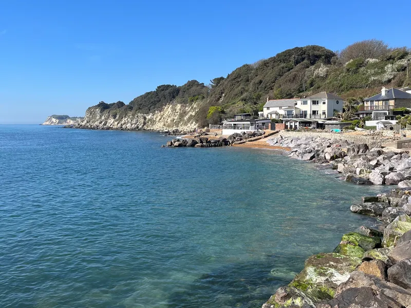 Steephill Cove shoreline with turquoise sea, rocky beach and white cliffs under a clear blue sky