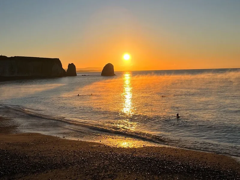 Sun setting over Freshwater Bay with sea stacks and golden reflections on calm water