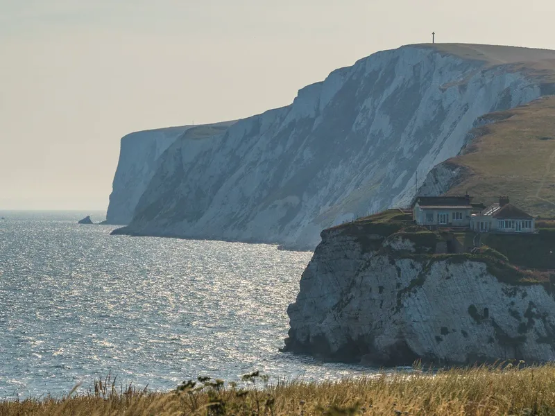 White chalk sea cliffs with a cliff-top house overlooking the ocean under a pale blue sky