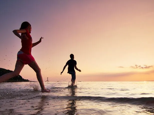 Two people running through shallow sea water at sunset on Colwell Beach