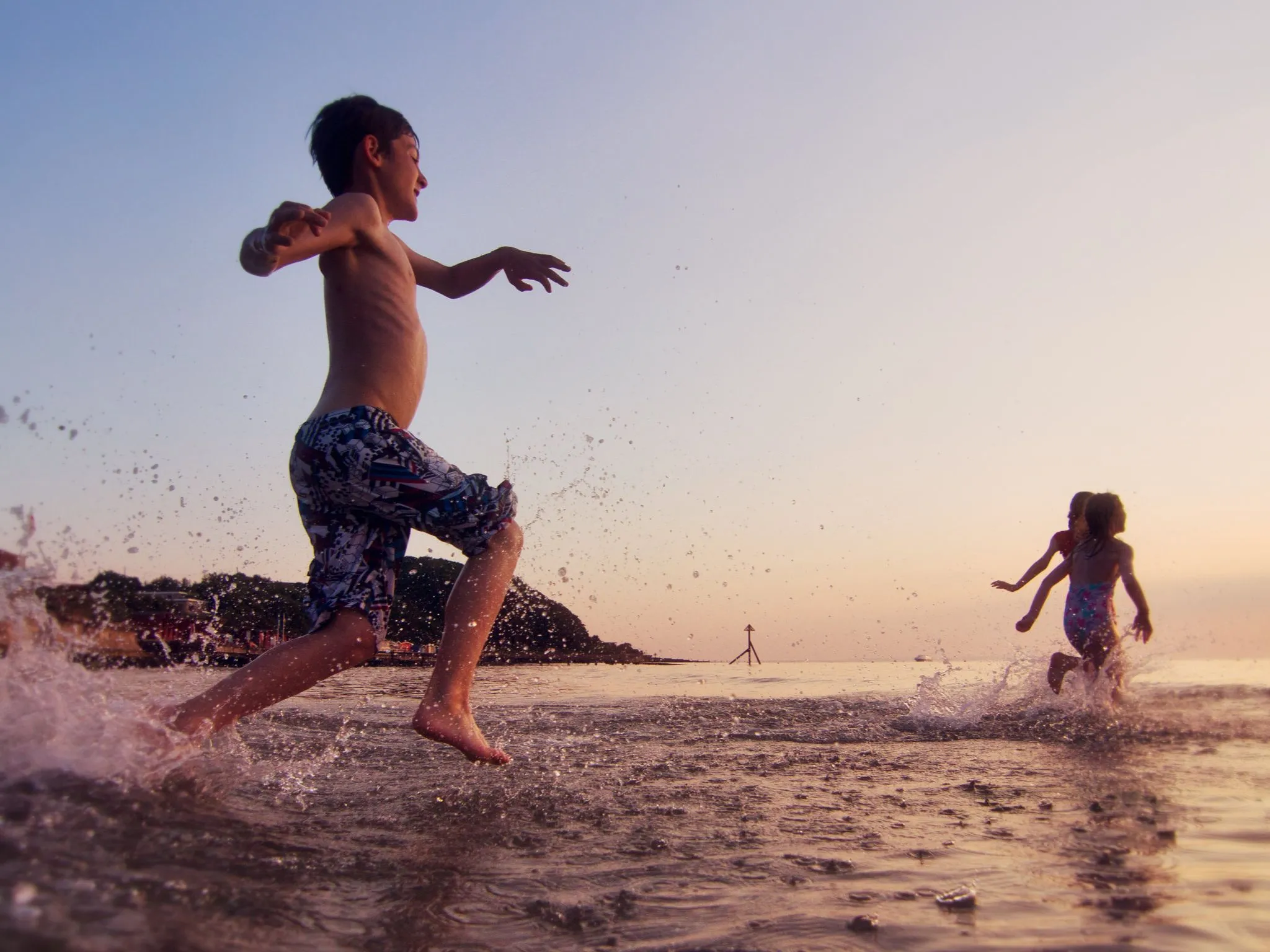 Child running through shallow sea water at sunset, splashing waves on a beach at Colwell Bay