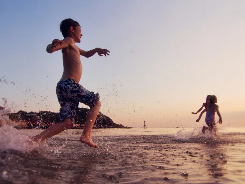 Child running through shallow sea water at sunset, splashing waves on a beach at Colwell Bay