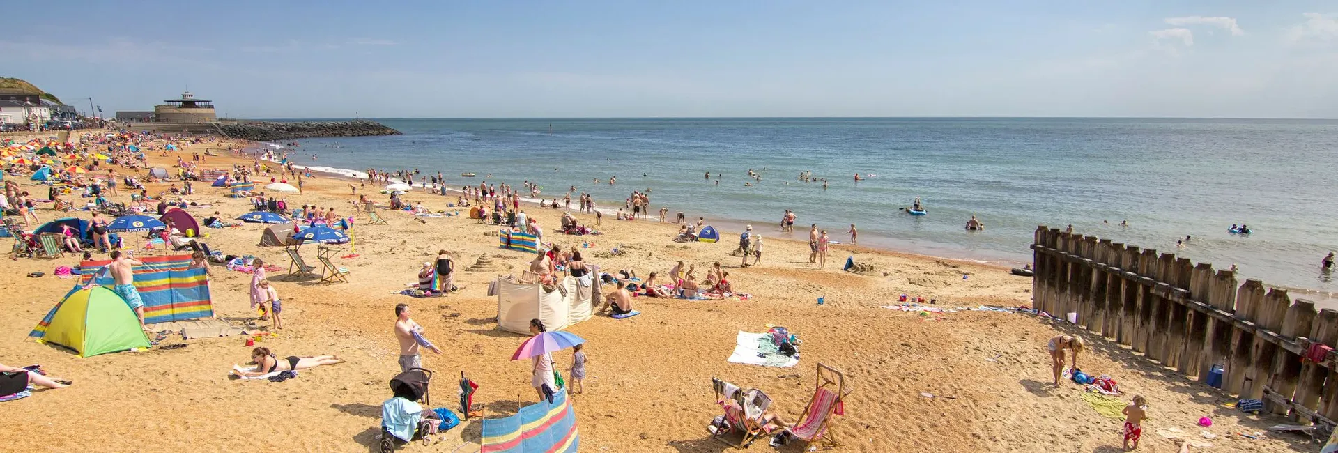 Crowded sandy beach at Ventnor with sunbathers, deckchairs and swimmers in the sea on a bright summer day