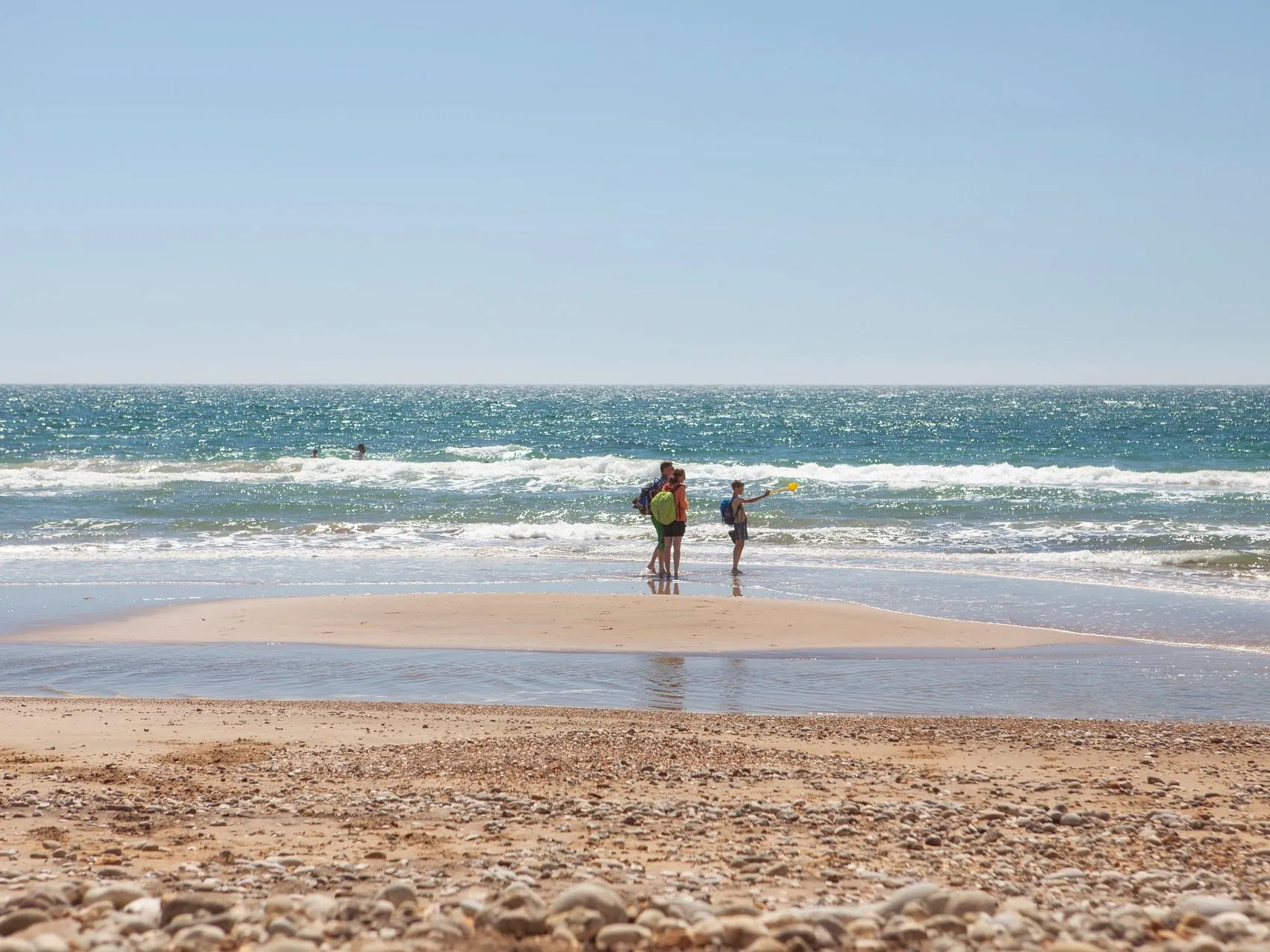 People standing by the shoreline at Compton Beach on a sunny day, with waves rolling in under a clear blue sky