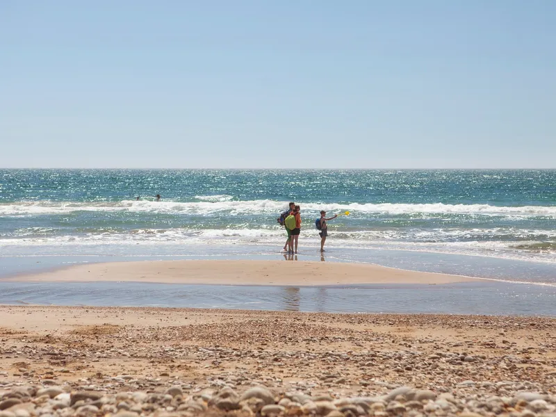People standing by the shoreline at Compton Beach on a sunny day, with waves rolling in under a clear blue sky