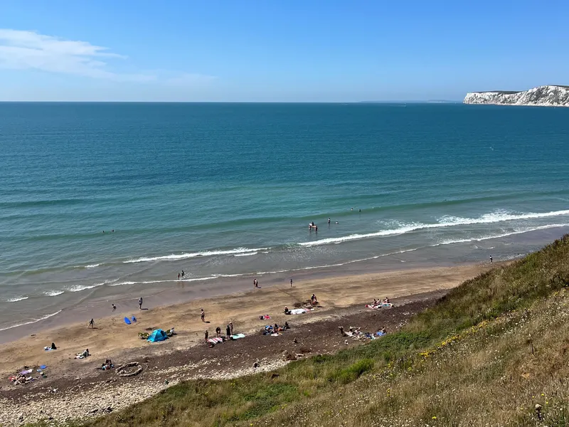 View over Compton Beach on a sunny summer day, with people on the sand, gentle waves and white cliffs in the distance