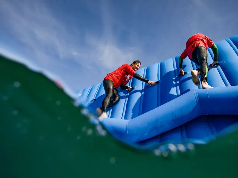 Two people climbing a blue inflatable obstacle at the Isle of Wight Aqua Park, seen from water level