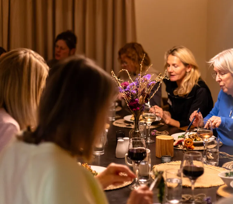 Group dining together at a long table under a warm pendant lamp, with flowers and wine glasses