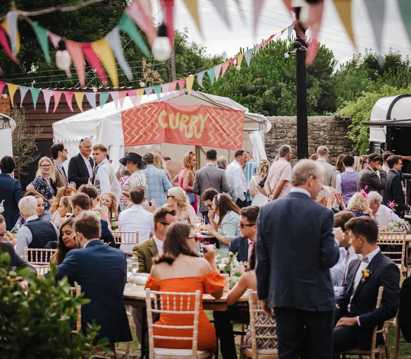 Guests gathered in a courtyard with bunting and a curry food stall
