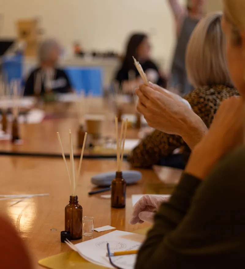 People seated around a table during a corporate activity, holding scent-testing strips beside small amber bottles.