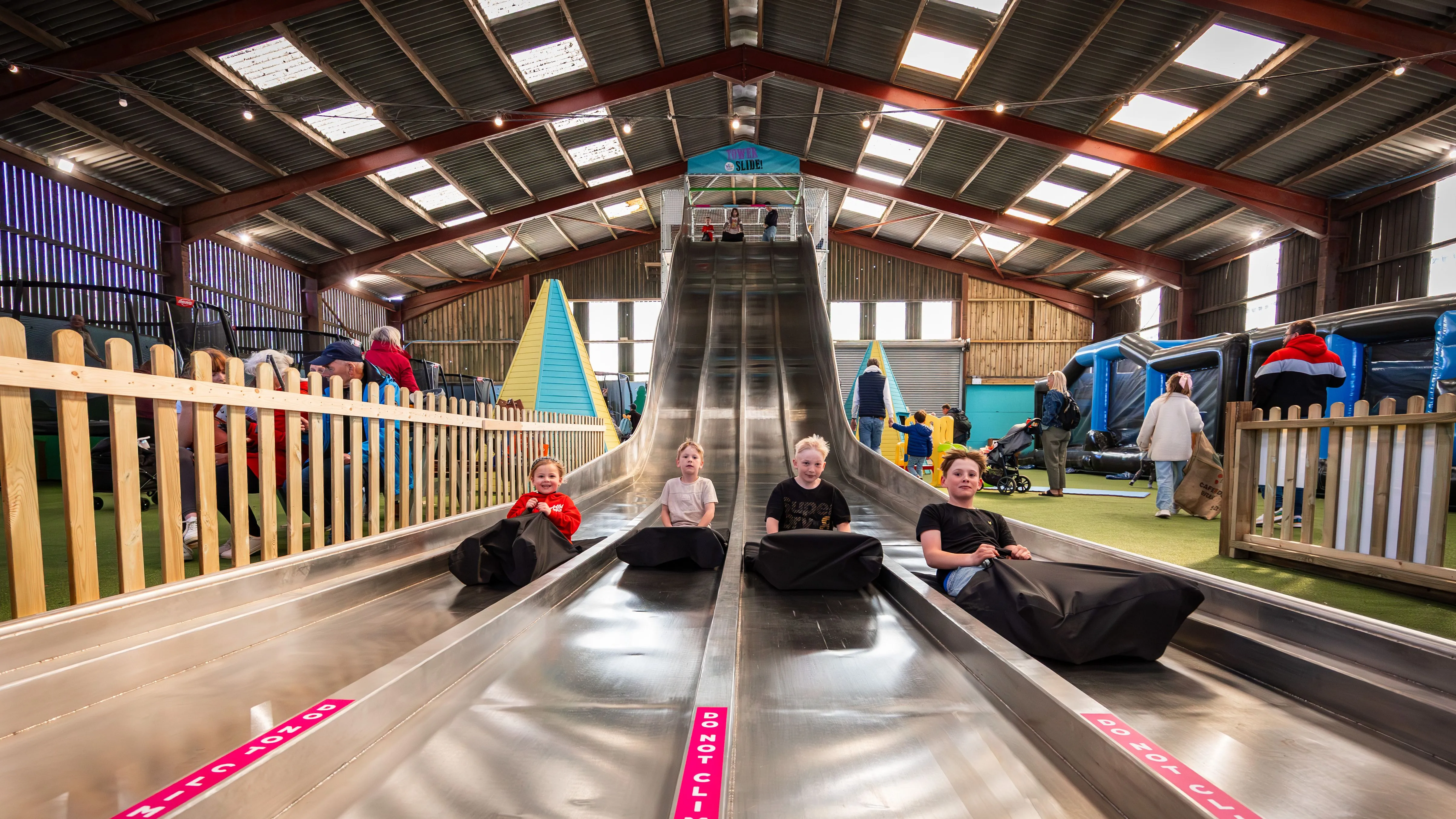 Children sitting on mats at the bottom of the Tower Slide inside Tapnell Farm Park’s indoor barn play area