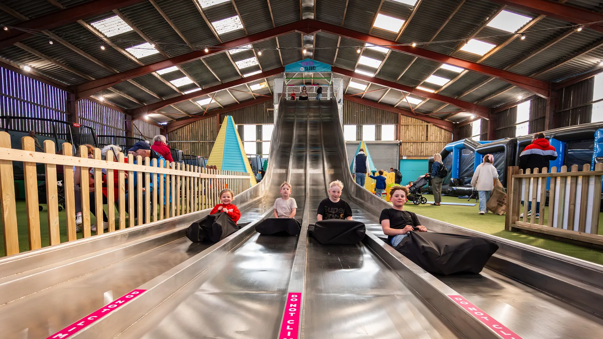 Children sitting on mats at the bottom of the Tower Slide inside Tapnell Farm Park’s indoor barn play area