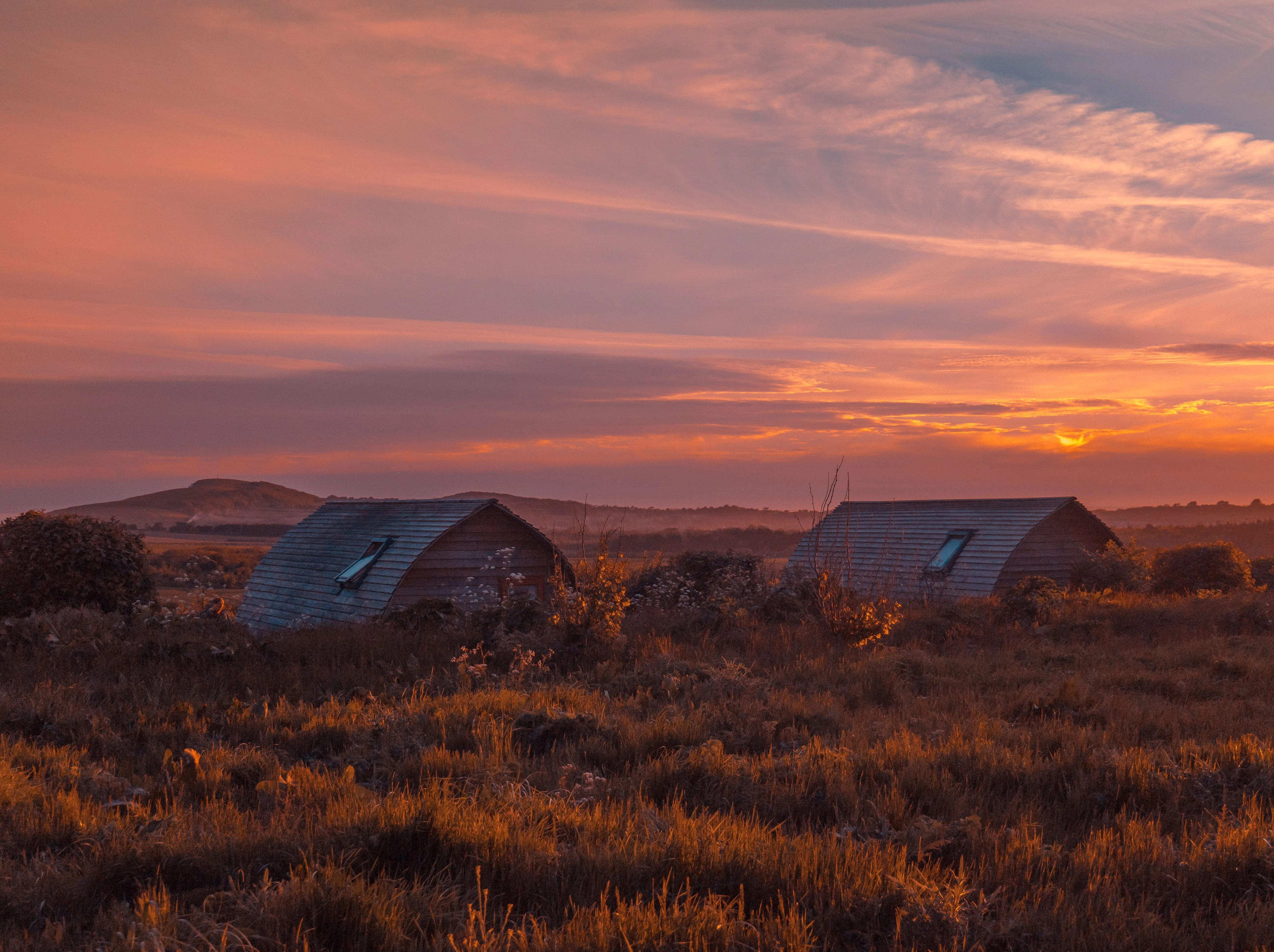 Two eco pods at Tapnell Farm silhouetted against a dramatic sunset sky