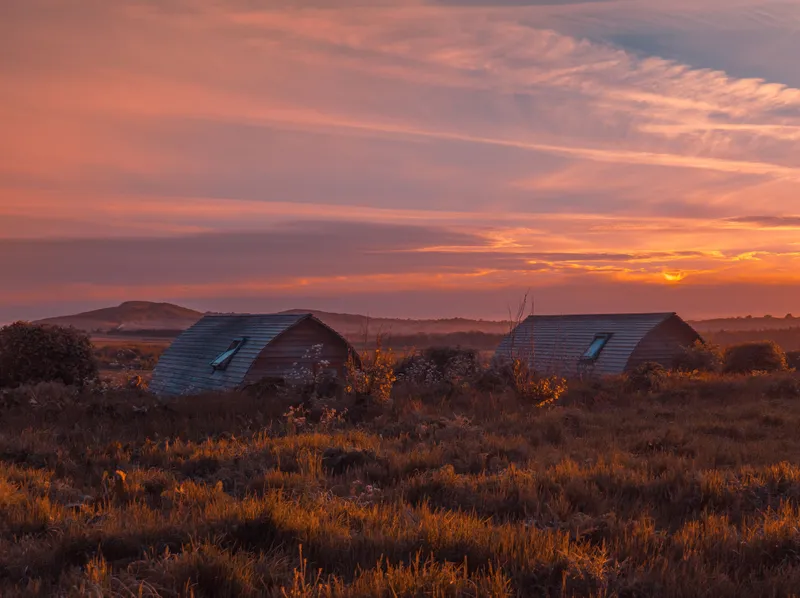 Two eco pods at Tapnell Farm silhouetted against a dramatic sunset sky