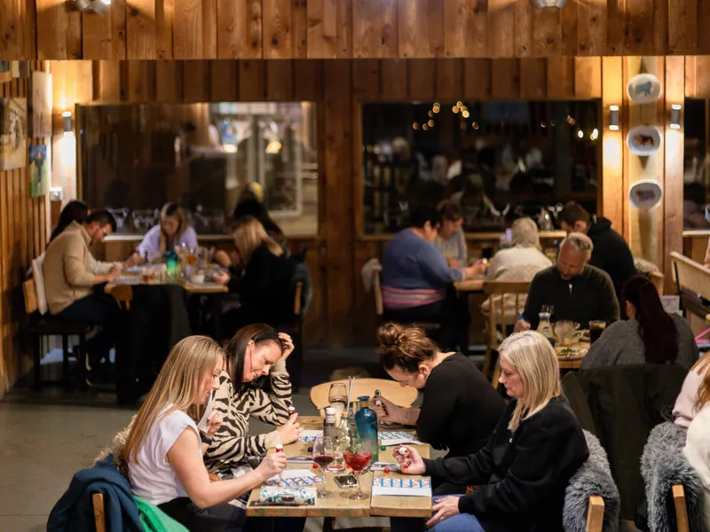 People playing bingo at long tables inside a rustic wooden barn, with cow head decorations on the wall