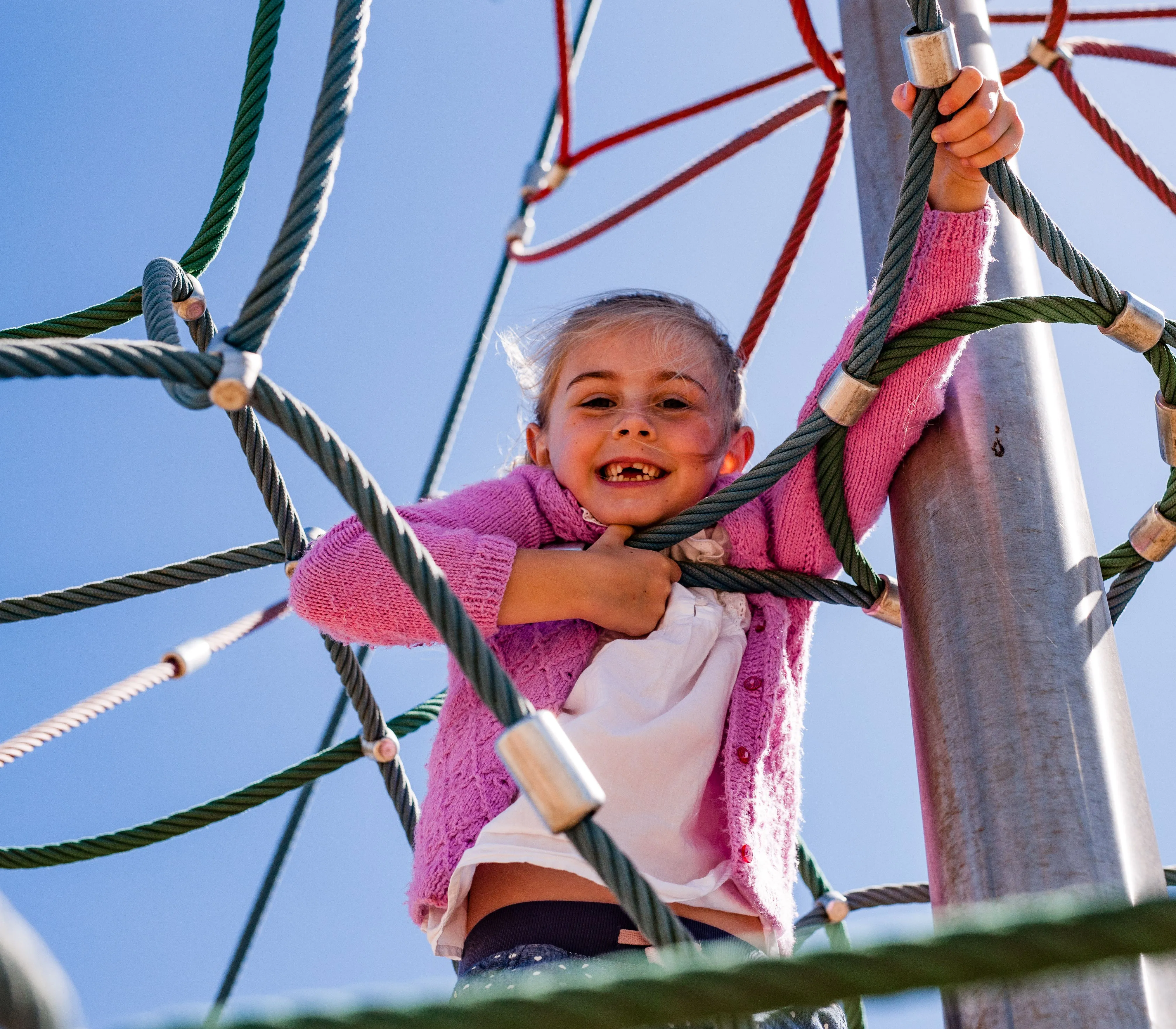 Smiling child climbing a rope web play frame under a clear blue sky