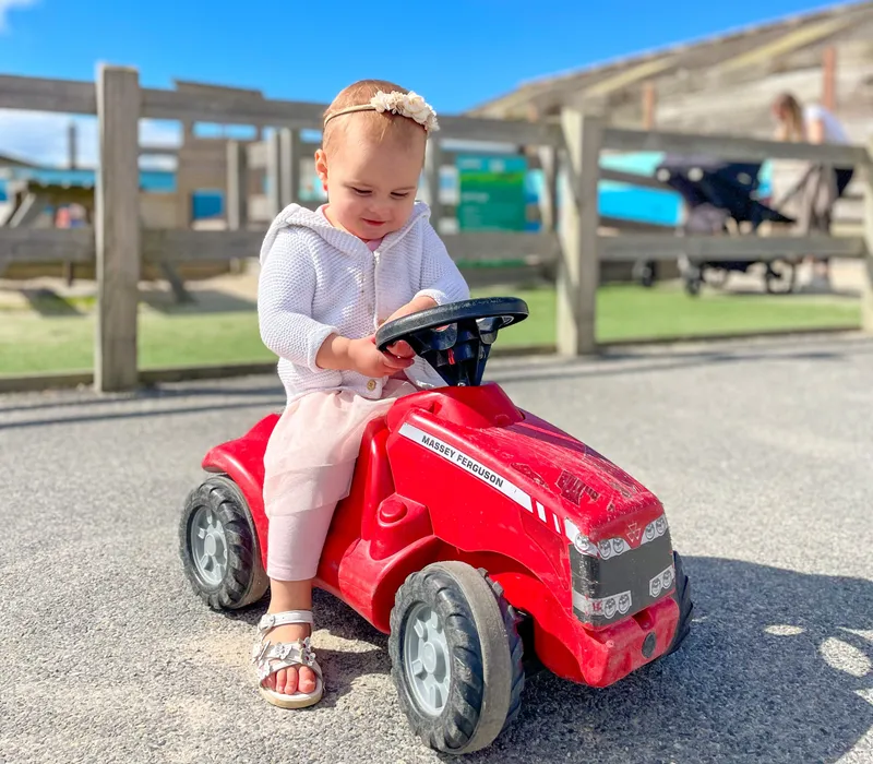 Toddler sitting on a red ride-on toy tractor outdoors under a bright blue sky