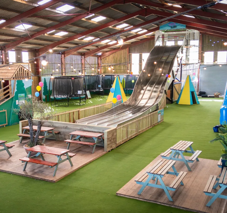Indoor play barn at Tapnell Farm Park with a tall tower slide, picnic benches and colourful decorations