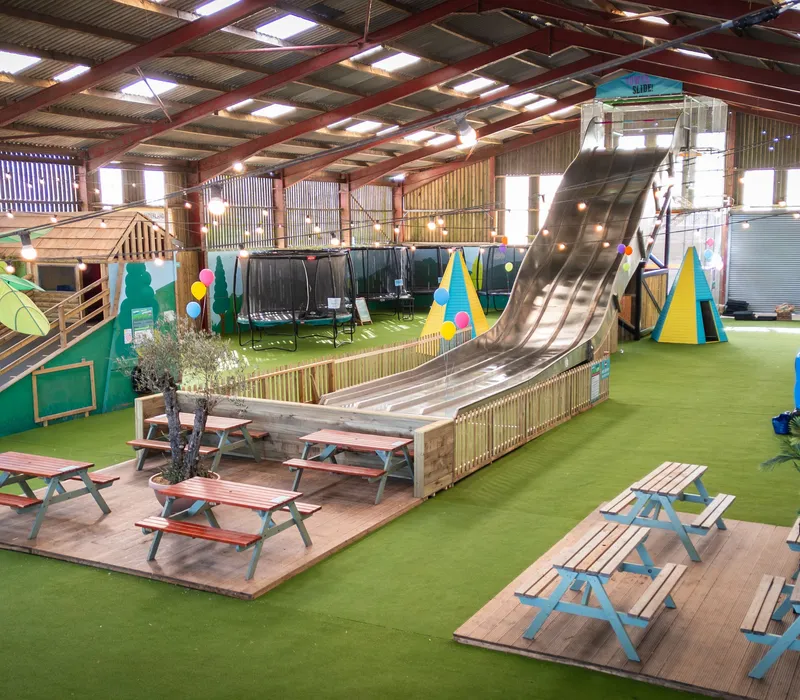 Indoor play barn at Tapnell Farm Park with a tall tower slide, picnic benches and colourful decorations