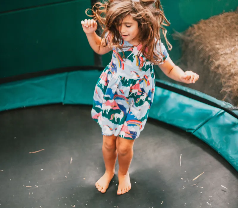 Young child jumping barefoot on a garden trampoline, wearing a colourful patterned dress