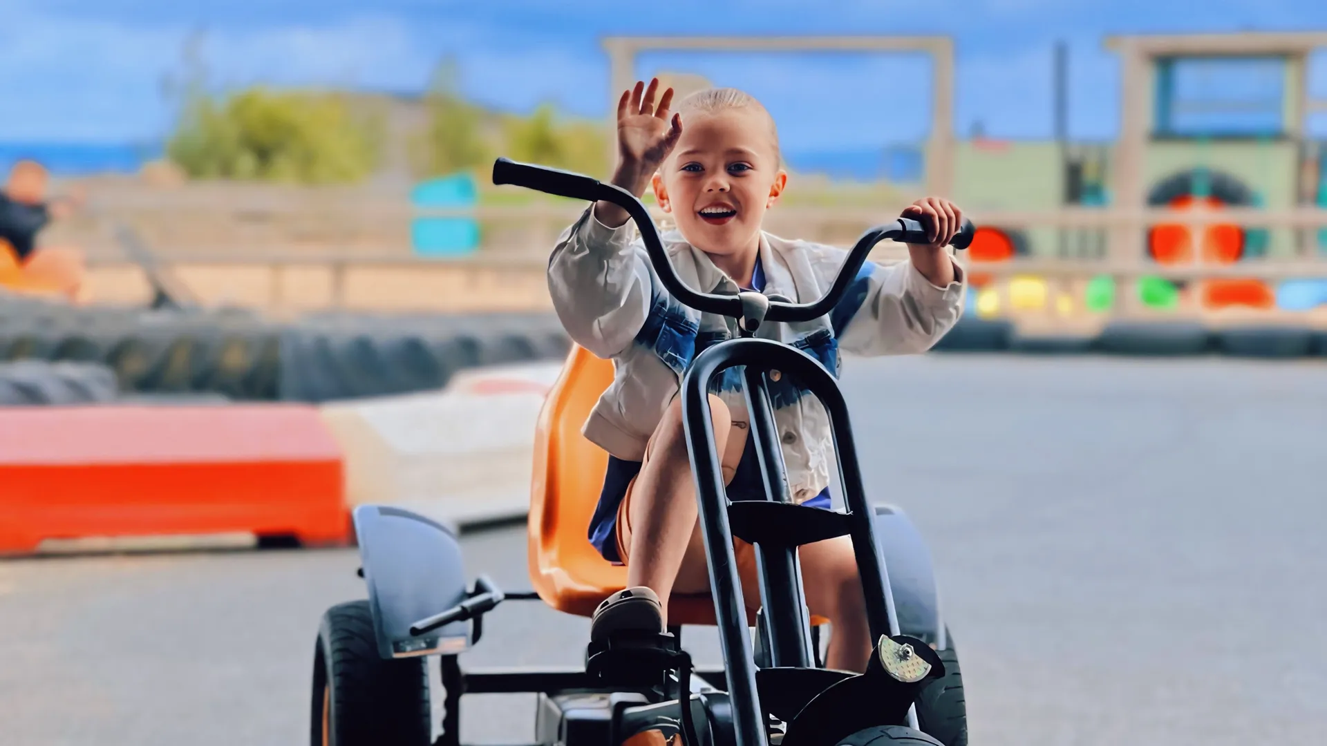 Child waving while riding a pedal go-kart on an outdoor track at Tapnell Farm Park