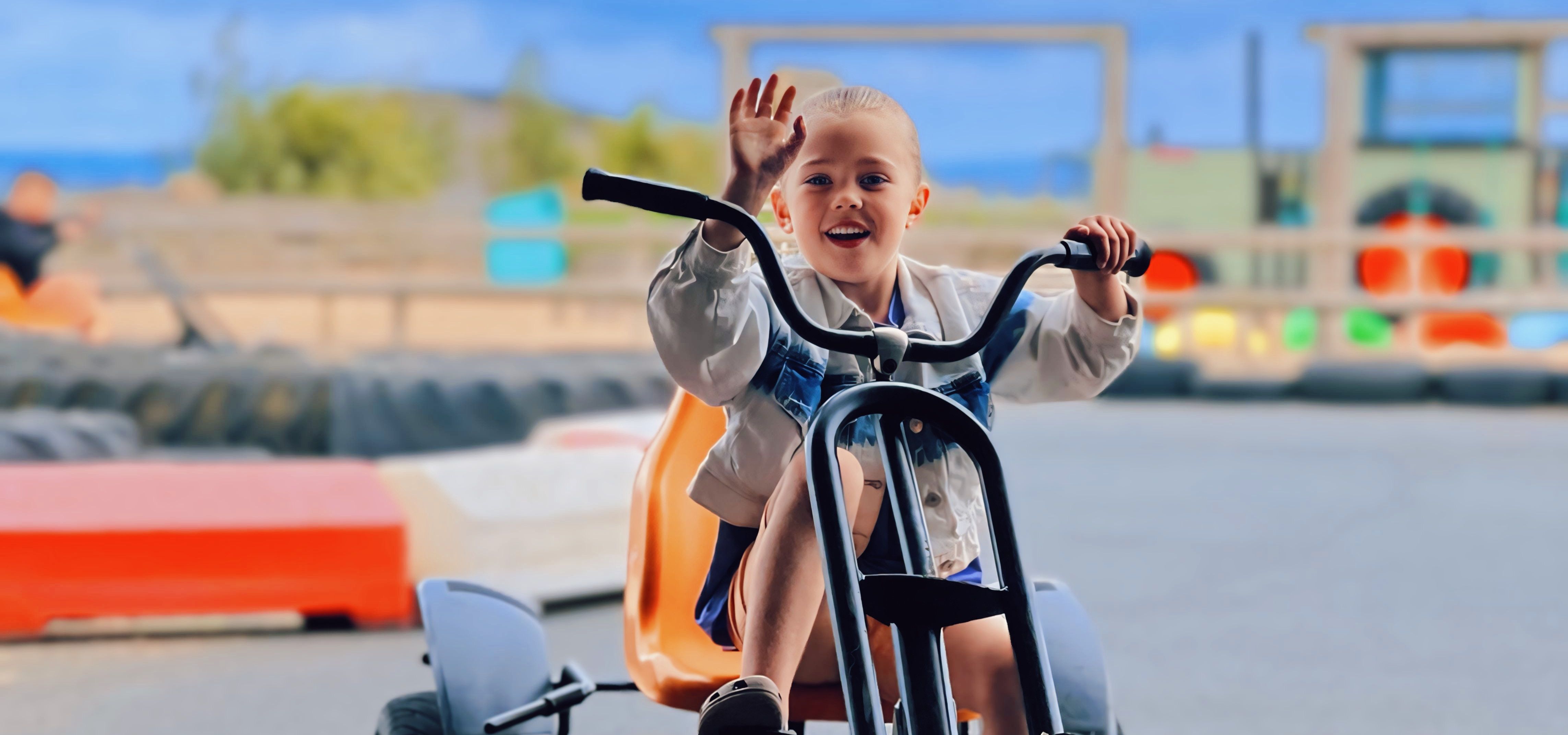 Child waving while riding a pedal go-kart on an outdoor track at Tapnell Farm Park