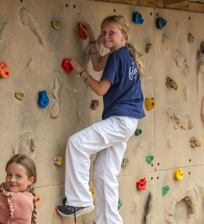Two children climbing a colourful indoor rock-climbing wall