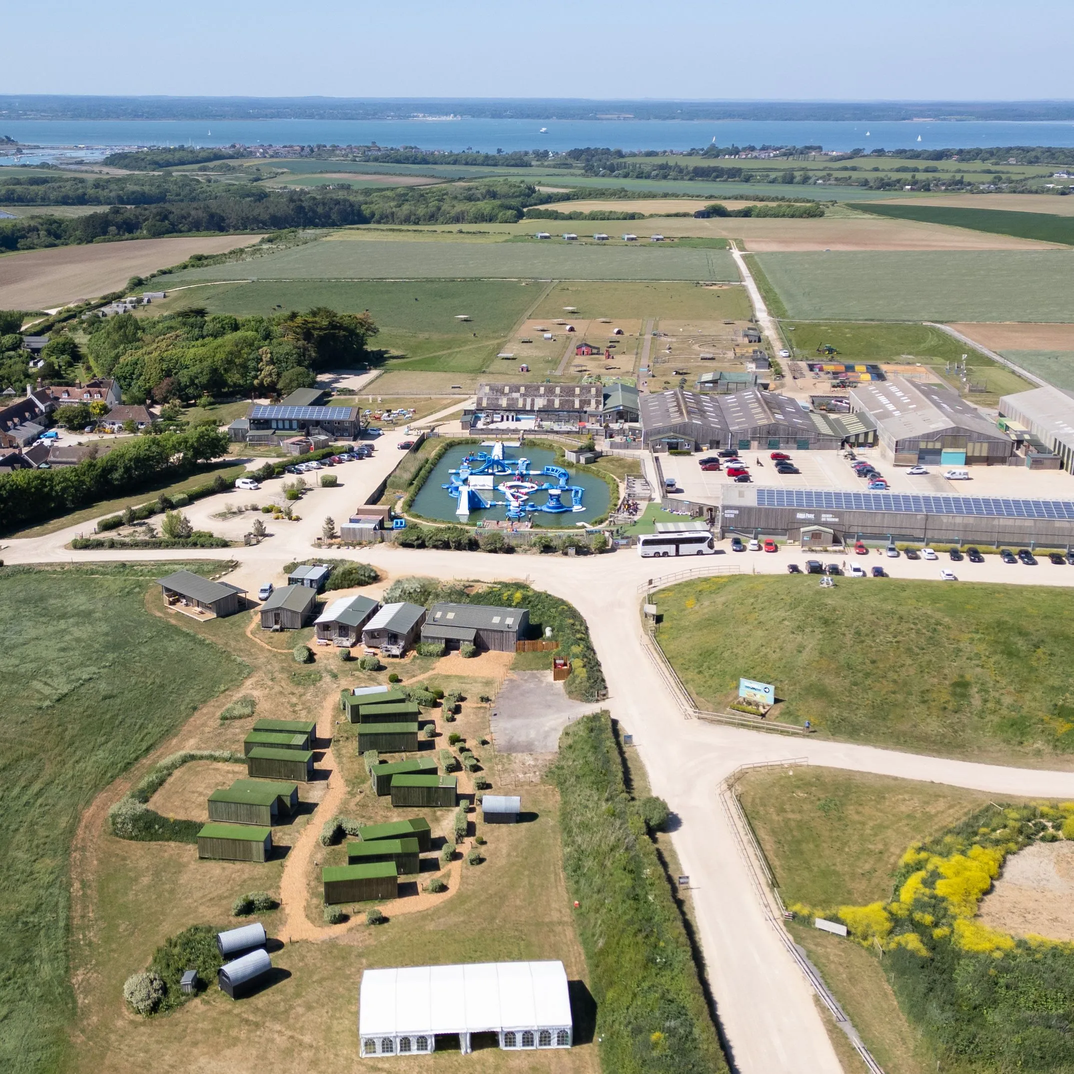 Aerial view of Tapnell Farm with cabins, farm buildings and an outdoor water park, surrounded by fields with the sea in the distance